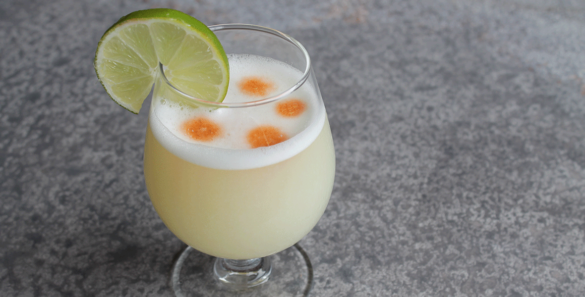 Clear glass holding a yellow drink topped with a lime.