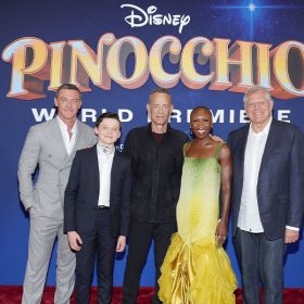 (left to right) Luke Evans, Benjamin Evan Ainsworth, Tom Hanks, Cynthia Erivo, and Robert Zemeckis attend the Pinocchio world premiere at Walt Disney Studios in Burbank, California. The group stands in front of a backdrop with the Pinocchio logo on it.
