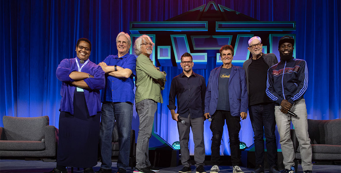 Carol Green, Bruce Boxleitner, John Scheele, Scot Drake, Donald Kushner, Mike Bonifer, and Juju Green stand next to each other on stage during D23 Expo at TRON's 40th anniversary panel