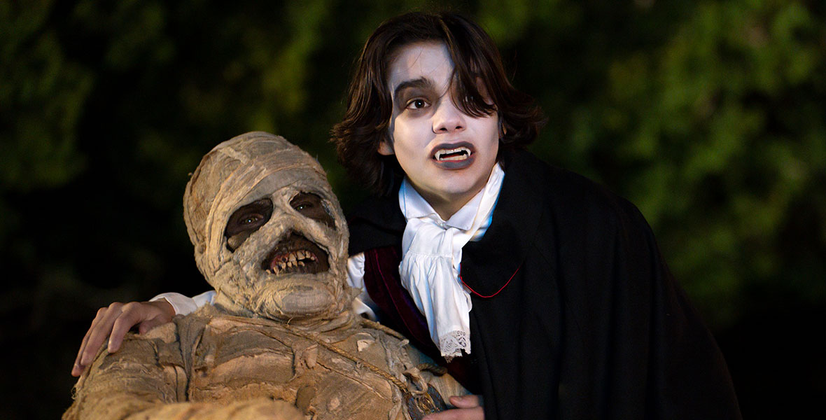 (From left to right): Phil Wright, in character as the mummy Harold, is bandaged and wearing an amulet. Malachi Barton, in character as Marshall, is wearing a vampire costume (including pointy teeth and a black cape) and is holding Harold upright.