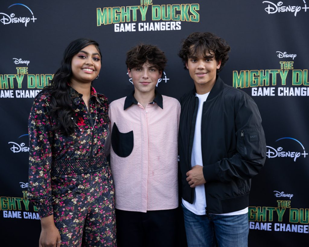 Actors Swayam Bhatia, Brady Noon, and Naveen Paddock stand on the purple carpet at the premiere event for the Season 2 The Mighty Ducks: Game Changers.