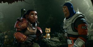 Izzy Hawthorn and Buzz Lightyear stand in a cave in their space suits. Behind them, Sox, the robotic orange cat, watches with wide eyes.