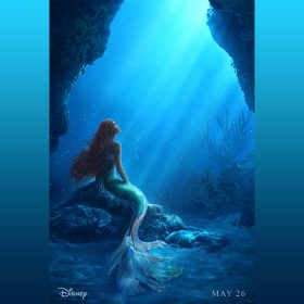 : In the new poster for Disney’s live action The Little Mermaid, Ariel (as portrayed by Halle Bailey) is underwater and sitting pensively on a rock, looking up towards sunlight streaming through the water to her right. Her tail is shades of green, pink, and white, and her long hair is red and in thin braids. Around her are rocks and underwater plant life; beneath it all is sand. On the left at the bottom of the poster is the “Disney” logo, and on the right it says “May 26.”