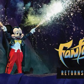 In a promo image for Fantasmic! returning to Disney’s Hollywood Studios at Walt Disney World Resort, Mickey Mouse is seen with sparks flying out of his fingertips. He’s wearing a sparkly black tailcoat, red pants, and a yellow bow tie. The logo for Fantasmic! is seen in the lower right of the image, and beneath it are the words “Returns November 3.”