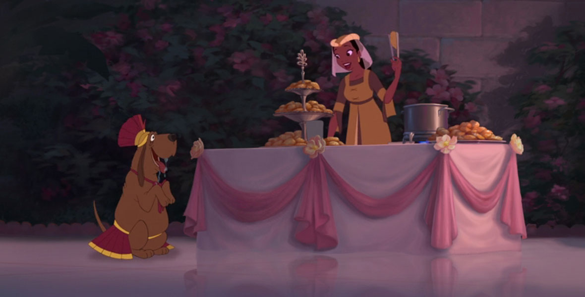 In a still from The Princess and the Frog, Stella, a brown basset hound dressed in a Roman solider costume, sits on her hind legs beside a table full of beignets. Tina stands at the table holding a beignet with some tongs, prepared to throw the treat for Stella to fetch.