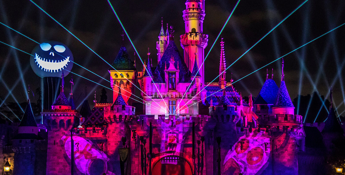 Sleeping Beauty Castle is lit up in pink and purple lights. Jack Skellington’s face is to the right of the castle.