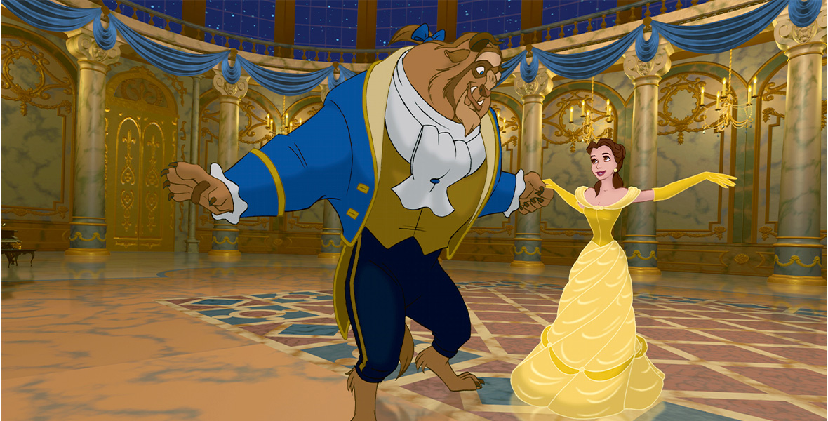 In a still from 1992’s Beauty and the Beast, the Beast is wearing his blue waistcoat and dark blue trousers, and Belle is wearing her iconic gold ballgown; the couple is dancing in the golden ballroom, holding hands. There is blue bunting hanging from the marble columns, and stars can be seen in the night sky through the windows at the top of the room.