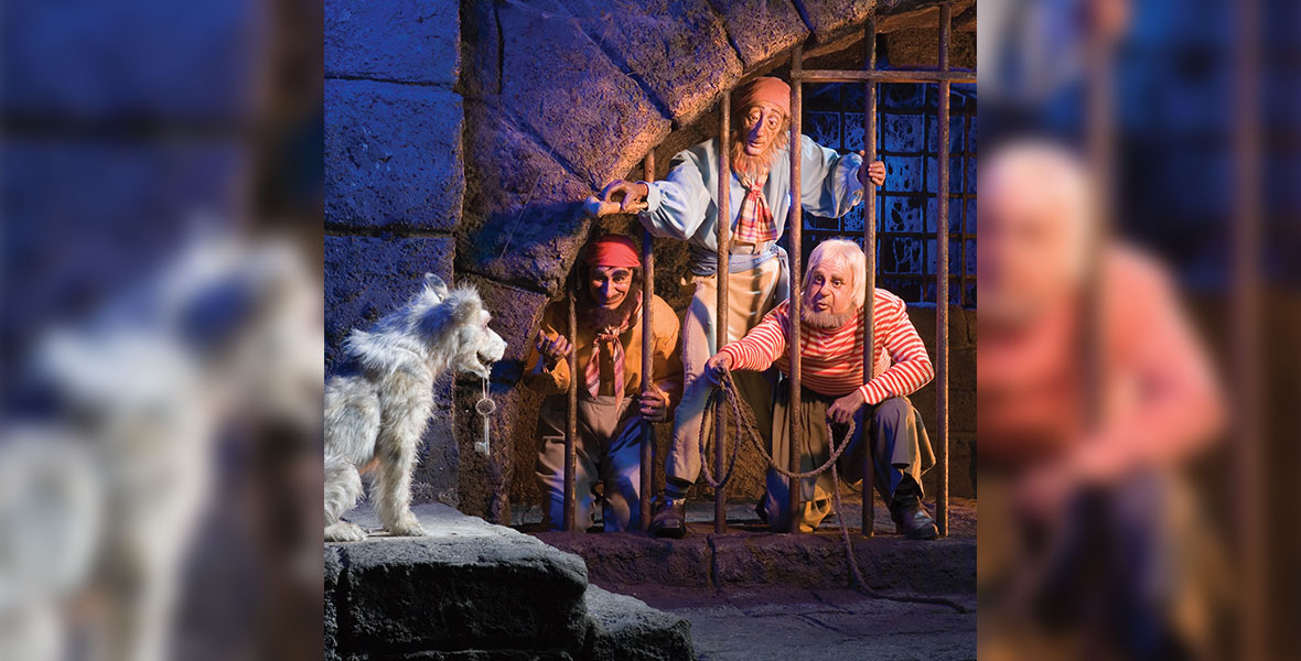 Three pirates from the Disneyland attraction Pirates of the Caribbean stand behind jail cell bars, all motioning or whistling towards a dog. The dog stands outside of the cell with the jail keys in its mouth.