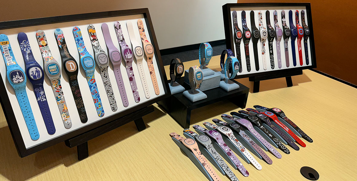 A display of all the Disneyland Resort MagicBand+ designs. Over a dozen bands sit in display boxes on a conference room table. There are special designs featuring princess crowns, the Disneyland “D”, a castle, Spider-Man, Nightmare Before Christmas characters, and Star Wars symbols.