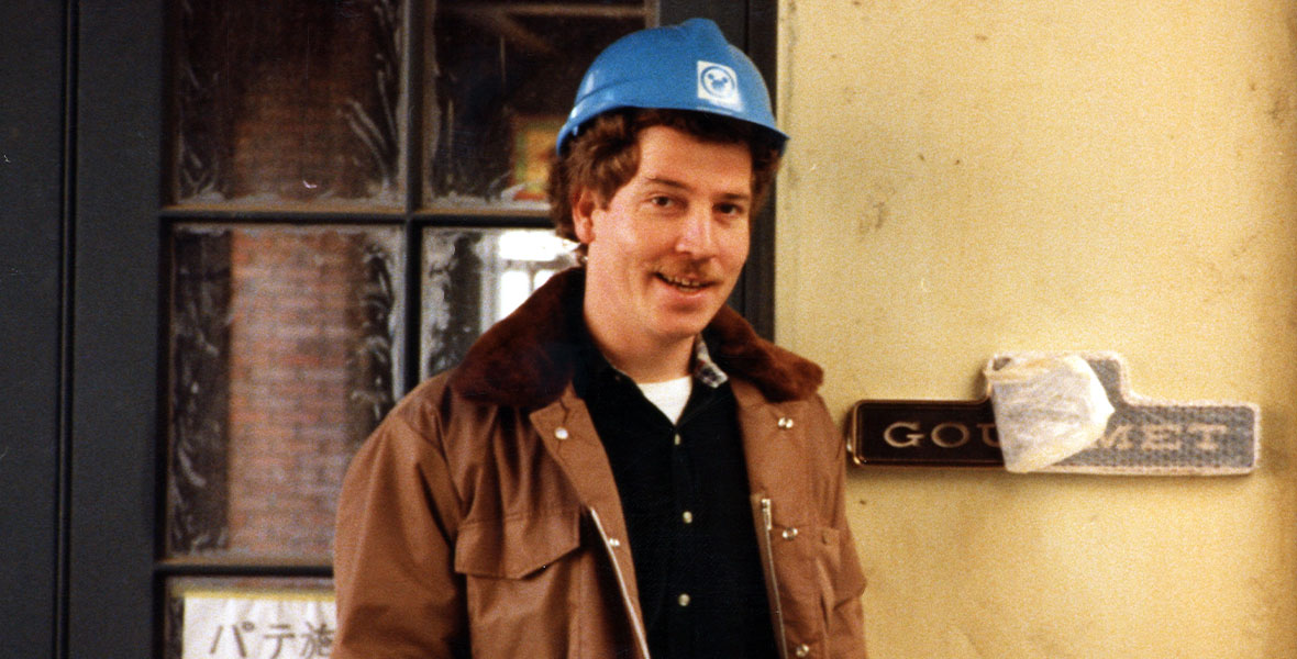 A young Bob Weis stands in a hardhat and construction clothing in front of a doorway within Tokyo Disneyland, during the construction of the theme park.