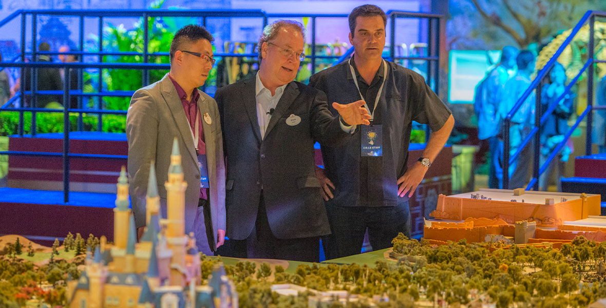 Bob Weis stands, flanked by two other men, behind a scale model of Shanghai Disney Resort in 2012. Weis is pointing to something outside the frame of the photo.