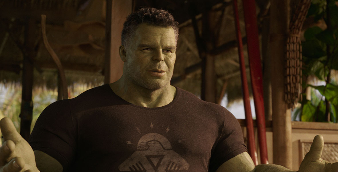 Mark Ruffalo in Hulk form. He is talking to his cousin, Jennifer, who is off screen on the right. The Hulk is wearing a basic black tee shirt with an eagle icon on the front in gray. He has both hands outstretched as he talks to Jennifer with a calm expression on his face. 