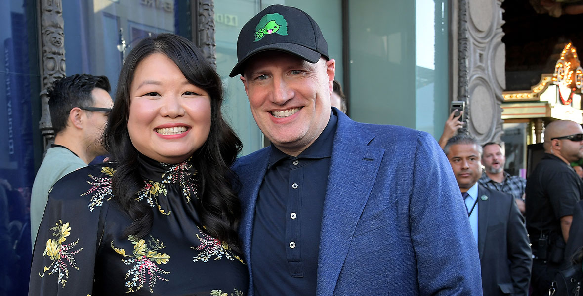 She-Hulk head writer and executive producer Jessica Gao with Marvel Studios president Kevin Feige, at the series’ premiere. Gao is wearing a black dress with a floral pattern on it; Feige is wearing a blue suit and a black baseball hat with She-Hulk on it.