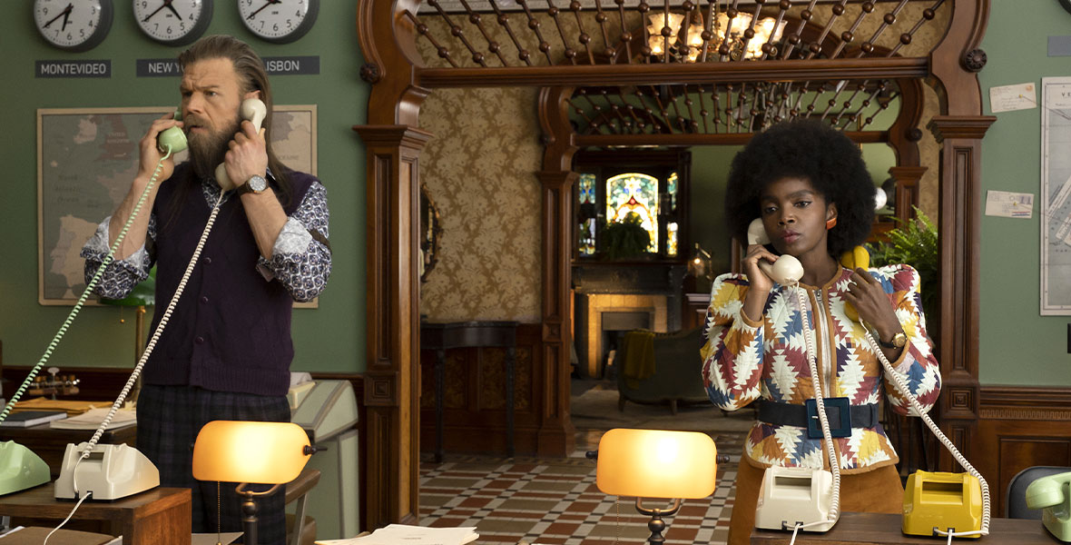 In a still from The Mysterious Benedict Society, from left to right, actors Ryan Hurst and MaameYaa Boafo are each speaking into two corded telephones.