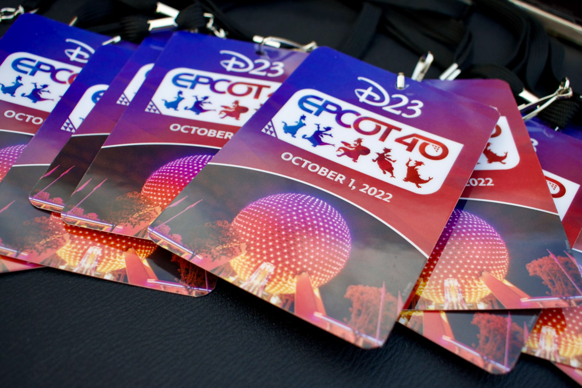Multiple EPCOT 40th event credentials laid out across a black tablecloth. The credential has a purple and pink gradient background featuring a nighttime photo of Spaceship Earth highlighted in the same colors. Above the photo is “October 1, 2022” written in white font. Above that is the EPCOT 40 logo with a while background; five different Figment silhouettes doing different poses drawn in blue, purple, and pink; and “EPCOT 40” above that. The D23 logo is seen at the top in white.