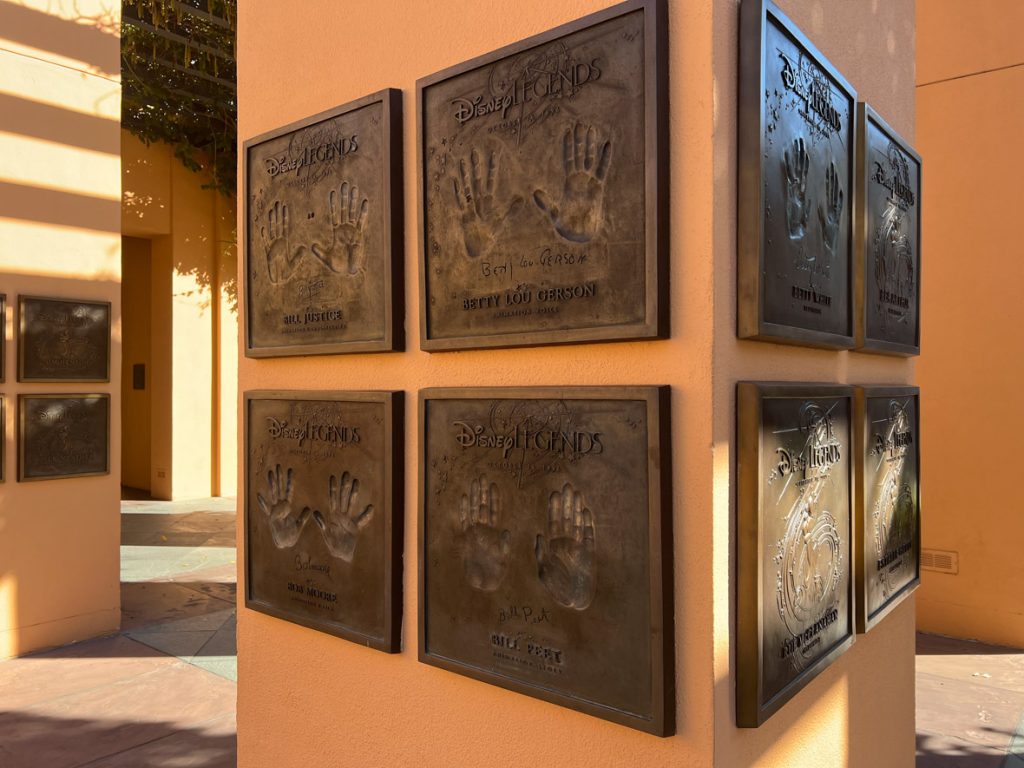 Eight Legends plaques of different Disney Legends and their handprints. The plaques are mounted on a tan pole.