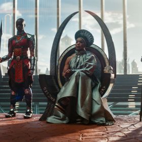 Ramonda, mother of T’Challa, sits on a throne in a silver dress and a circular silver headpiece.