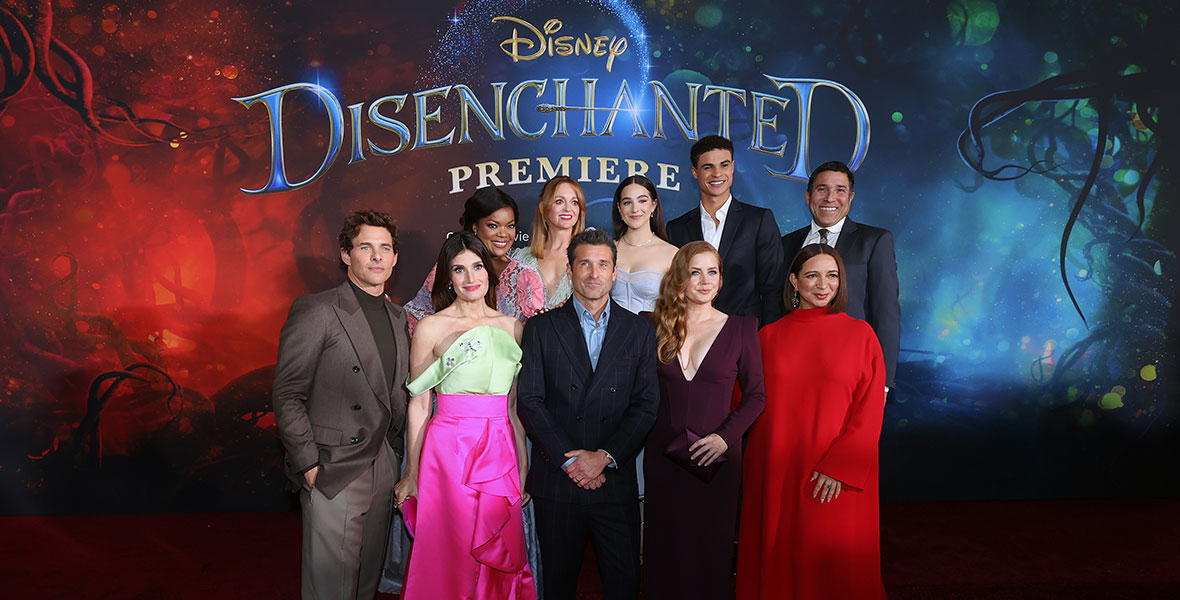 The cast of Disenchanted poses in a group photo in front of a sign for the film’s world premiere 