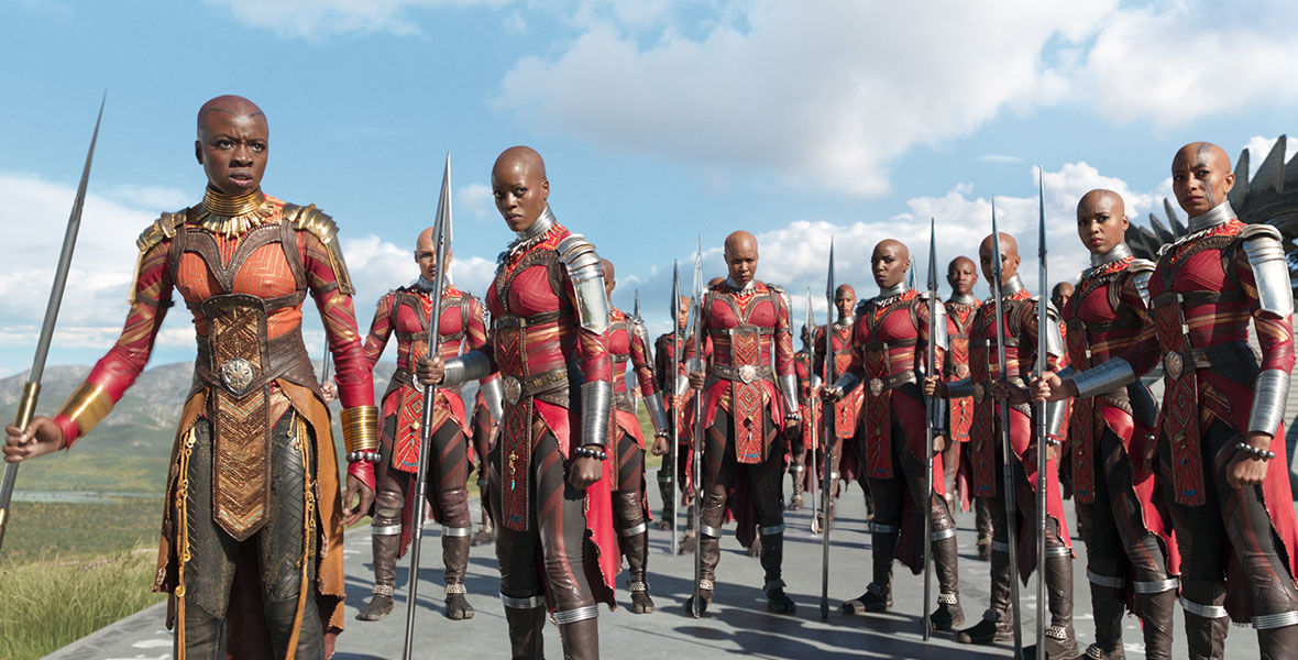 The Dora Milaje, the personal security of the Black Panther as well as Wakanda’s defense, stand in matching red and orange uniforms with large spears.