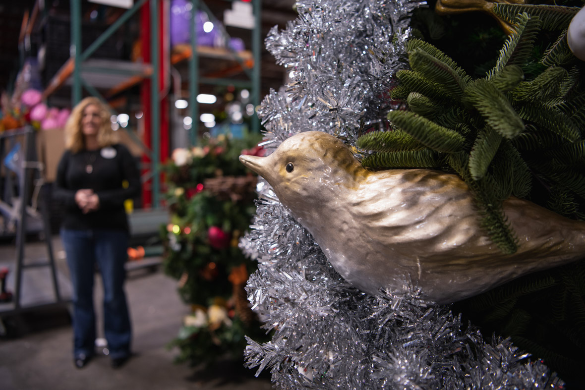 Dawn Pipal-Keehne, Resort Enhancement Area Manager for Disneyland Resort, is seen in the background, while in the foreground is a golden bird ornament, hanging from a Christmas tree in the Resort Enhancement warehouse in Anaheim, California.