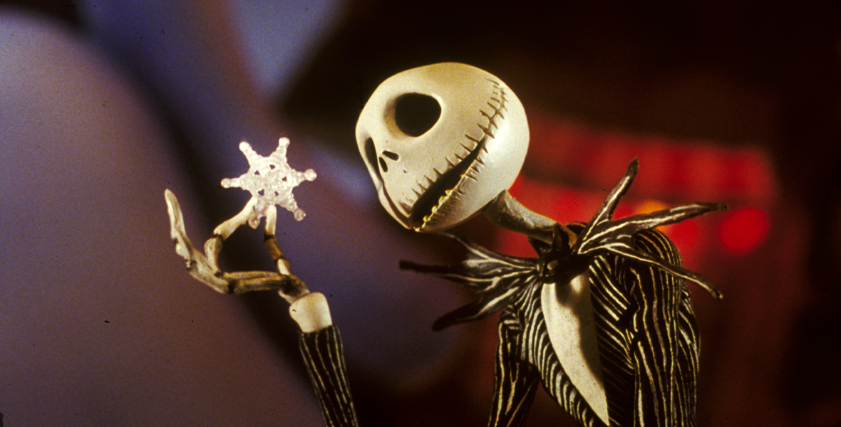 Jack Skellington is a skeleton in a black and white pin-striped suit. He holds up a large snowflake and looks at it.