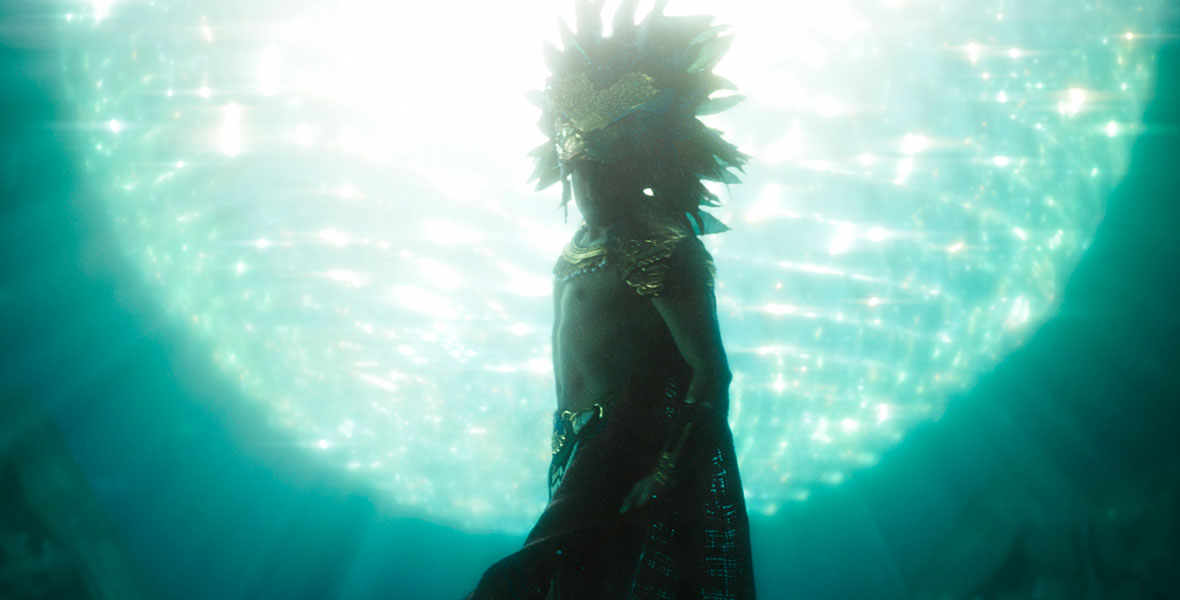 In a still from Black Panther: Wakanda Forever, Namor (Tenoch Huerta Mejía) is underwater. He wears a gold headdress and jewelry.