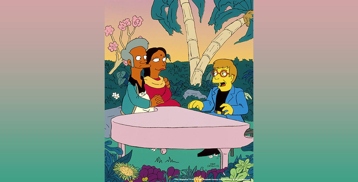 In a scene from the animated series The Simpsons, a cartoon version of musician and Disney Legend Elton John sits at pink piano in a colorful garden. John wears a blue suit, red-framed glasses, a black T-shirt, and black shoes. A man and a woman sit on the opposite side of the piano and hug while looking at John. The man wears a black button-down shirt, green jacket, and white pants. The woman wears a magenta dress and yellow scarf draped on her neck and shoulders.