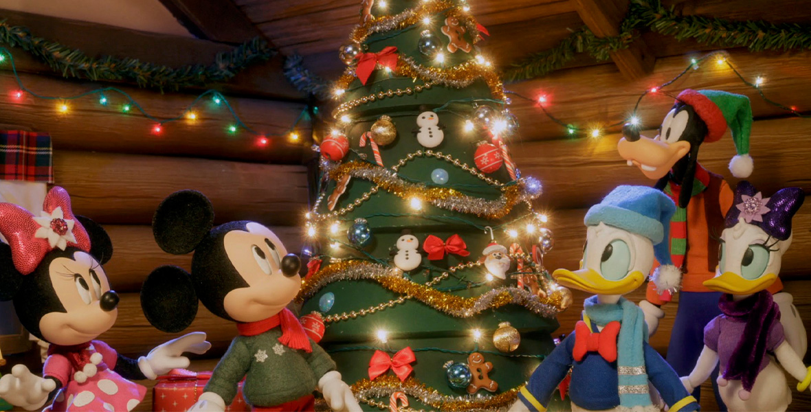 In the stop-motion holiday special Mickey Saves Christmas, Minnie Mouse, Mickey Mouse, Donald Duck, Goofy, and Daisy Duck stand around a green Christmas tree adorned with gold tinsel, Christmas ornaments, and lights. Green garland and multi-colored lights are strung around the room near the ceiling.