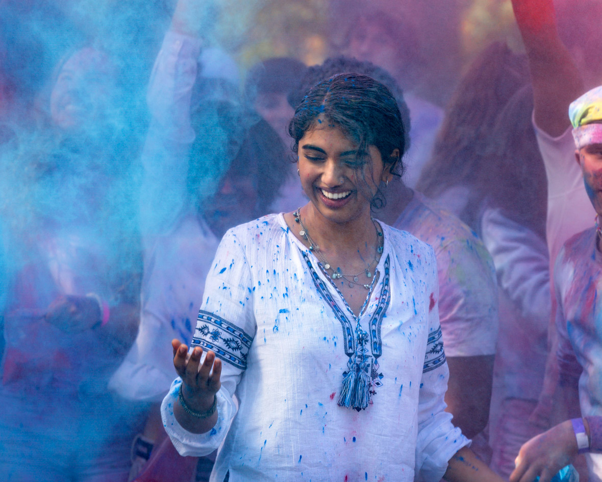 In this scene from Spin, Rhea (Avantika) is smiling and wearing a white and blue top. Colorful powder is in the air, and it’s staining her hair, skin, and clothes.