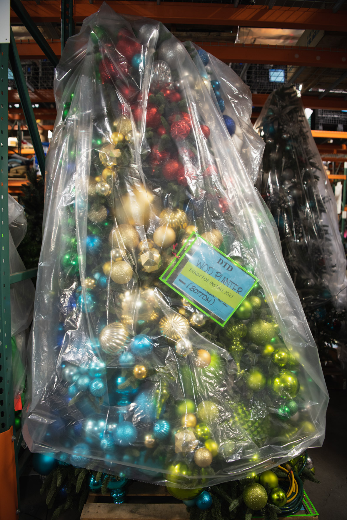 Christmas garland decorated with round silver, green, and blue ornaments is bunched up in a giant plastic bag that’s hanging in the Resort Enhancement warehouse in Anaheim, California. The bag is labeled “Ready for Install 2022.”