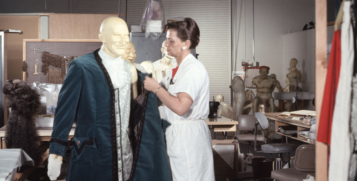 In a photograph from the mid 1960s, Alice Davis stands in an Imagineering workroom next to a mannequin dressed in a costume for Disneyland’s Pirates of the Caribbean attraction.