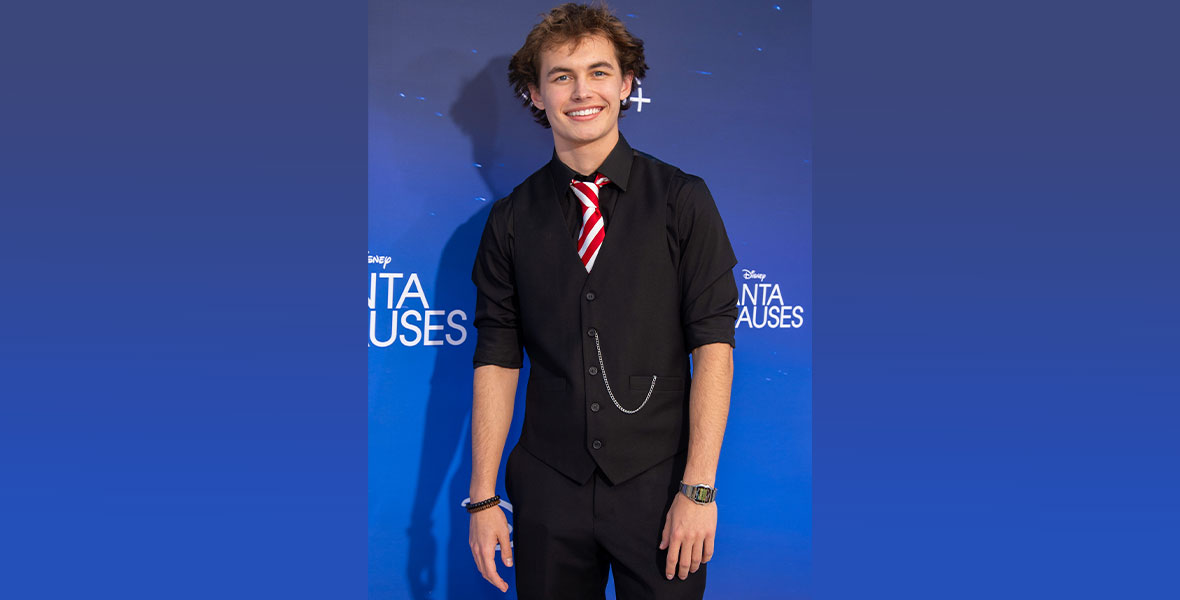 Actor Austin Cane poses in front of a dark blue backdrop with Disney+ and The Santa Clauses branding.
