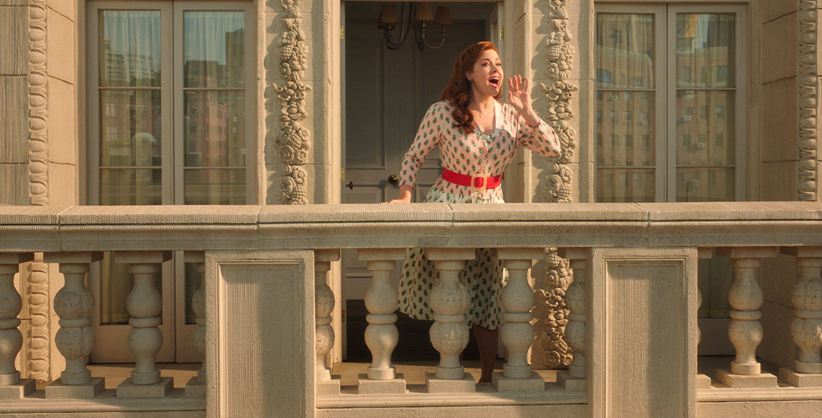 Giselle stands on her balcony with a hand up to her mouth as she calls out a song.