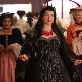 Rosaleen and Ruby flank Malvina as they all walk through a crowded room. Malvina is dressed like an evil queen, while Rosaleen and Ruby both wear simpler gowns and hats.