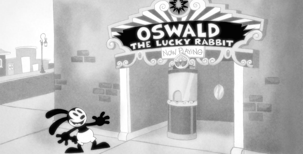 The black and white animated character Oswald the Lucky Rabbit stands outside a brick movie theater with a smile on his face, his arms outstretched, and his rabbit ears leaning back. An art deco marquee says Oswald the Lucky Rabbit Now Playing. There is a ticket window and two doors just below the marquee.