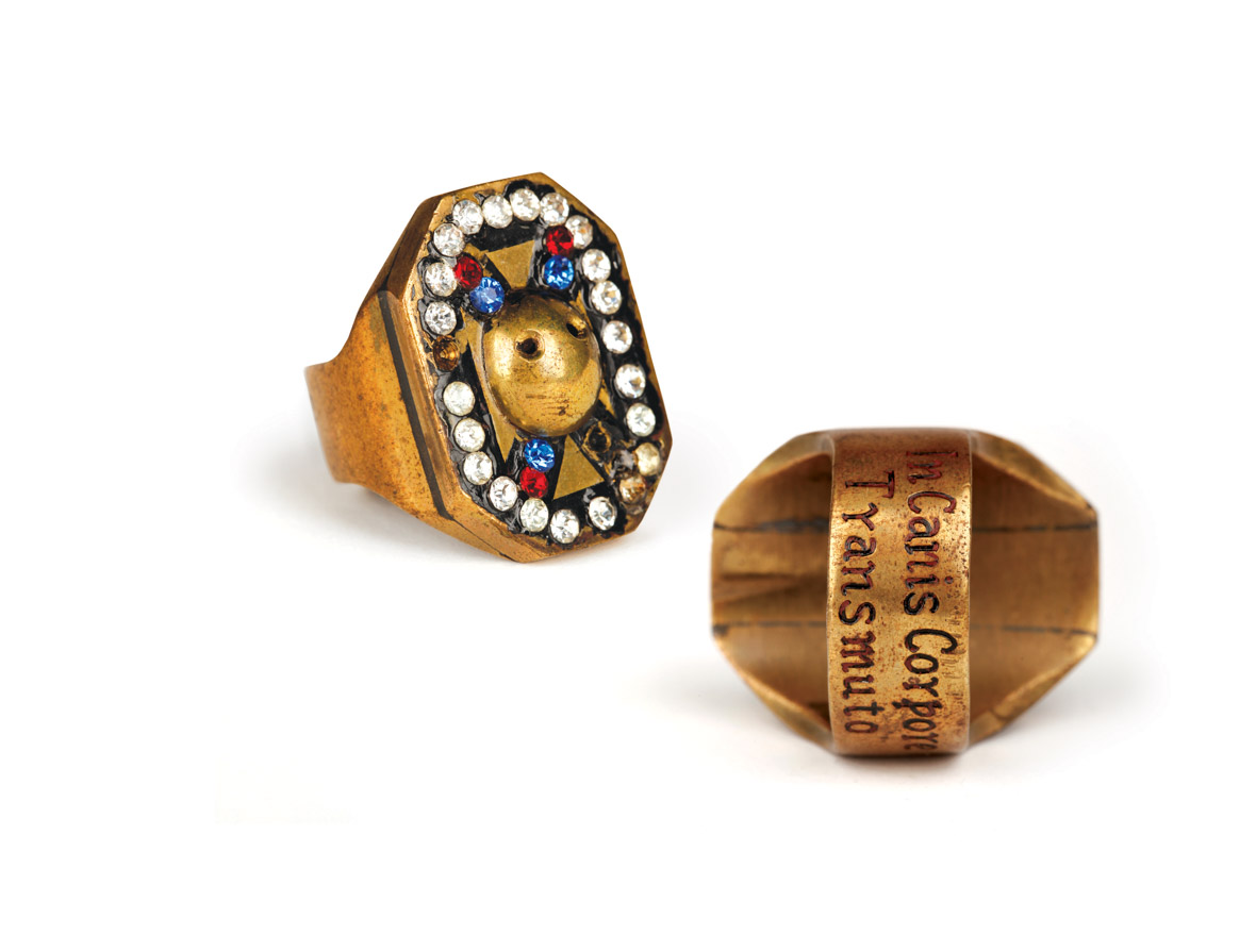 A photo depicts two views of the magic ring used in the Disney film The Shaggy Dog, showing the outside of the ring and inscription inside the ring. The ring is one of the historical artifacts that will be included in Disney100: The Exhibition, and has been photographed against a neutral white background.