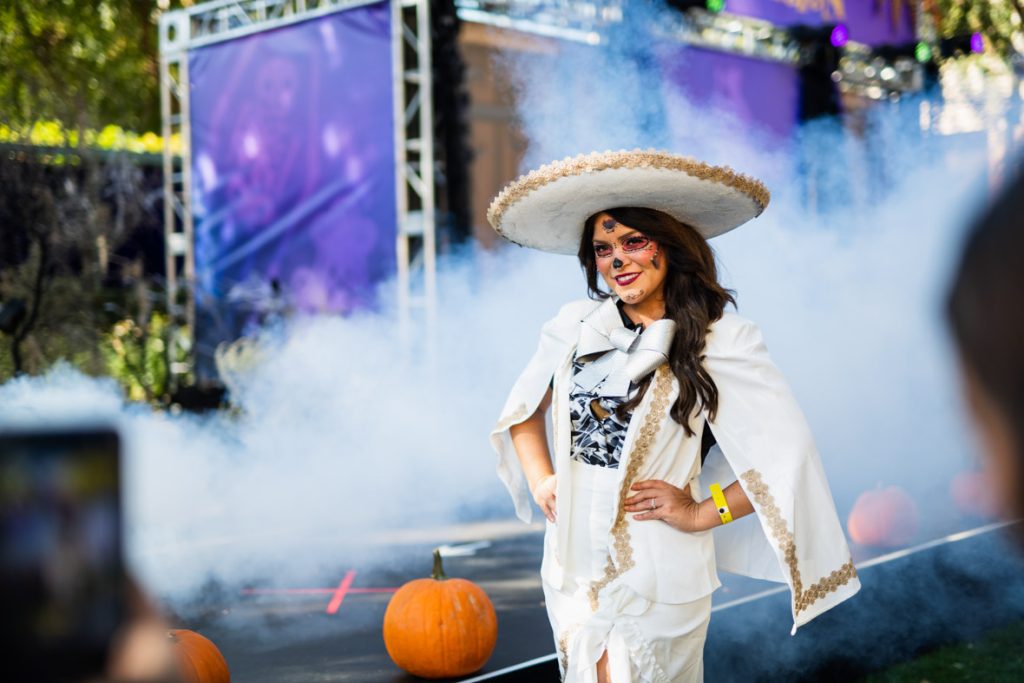Guest dressed as Ernesto De La Cruz from Coco. They’re wearing a white and gold sombrero, white and gold cape and pants, and white skeleton shirt. The guest also has skeleton-like makeup in red, white, and black.