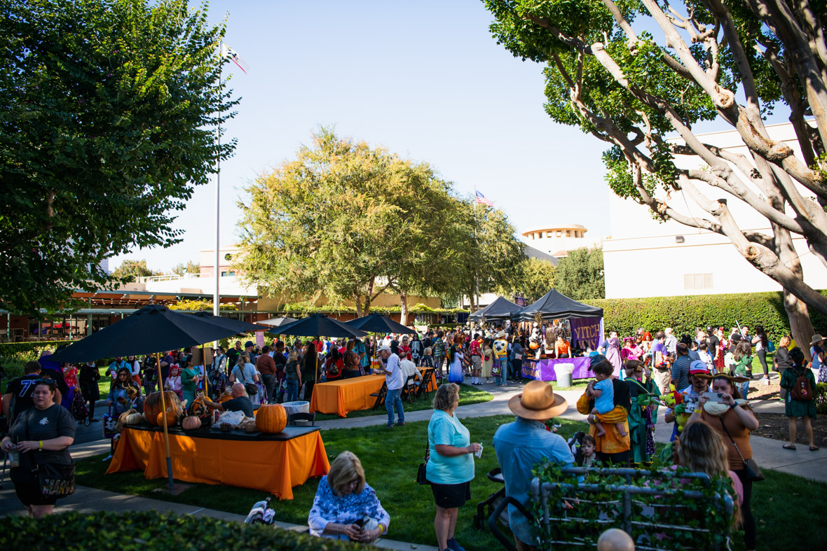 Wide overview of the Studio Lot filled with guests, black umbrellas, and booths with orange tablecloths.