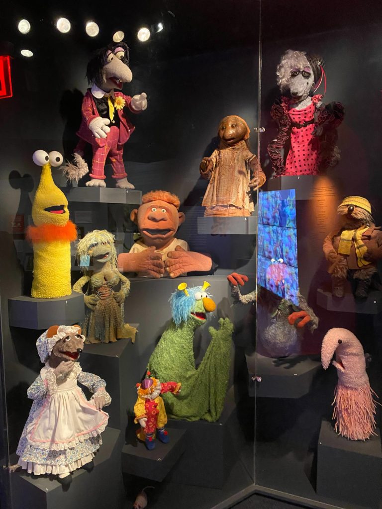 A variety of Muppets are displayed on varying levels in a glass display box.
