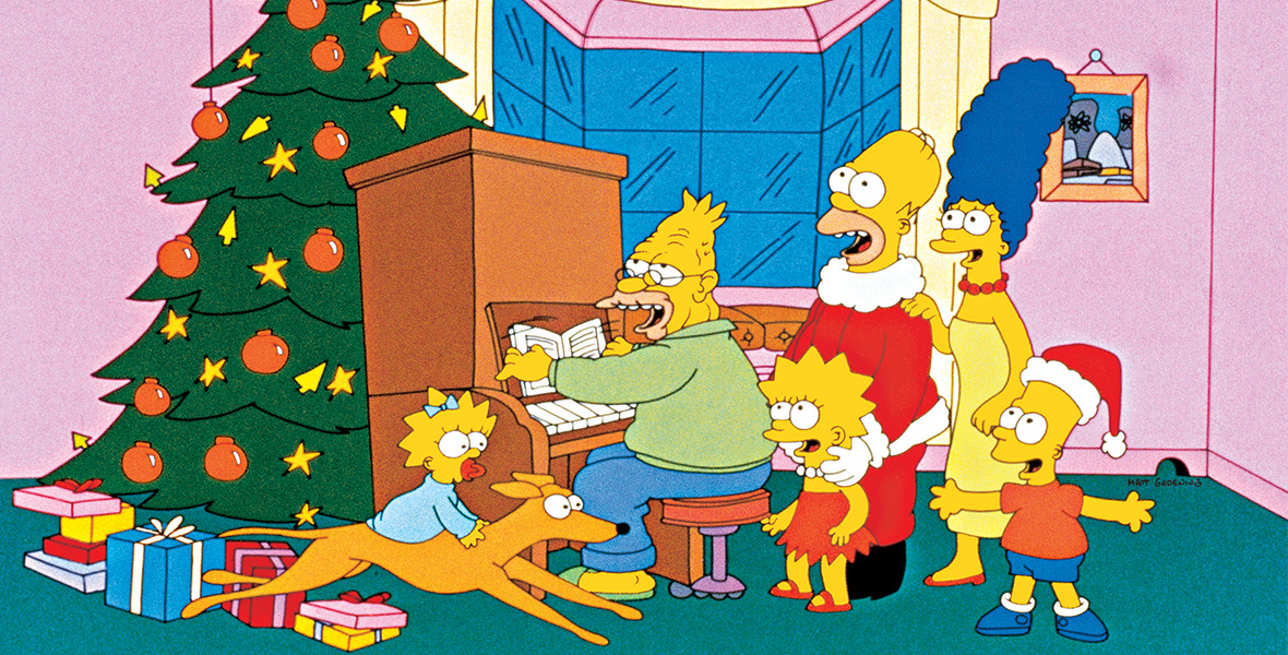 In a scene from a holiday-themed episode of The Simpsons, the animated family—Maggie, Santa’s Little Helper, Grandpa, Lisa, Homer, Marge, and Bart—stand around a large brown piano and sing. Behind the piano stands a large green Christmas tree with a gold star on top and decorated with round, red ornaments, and a strand of gold lights. Homer is dressed as Santa Claus in a red suit with white fur and black boots. Bart wears the red Santa Claus hat with white fur atop his head.