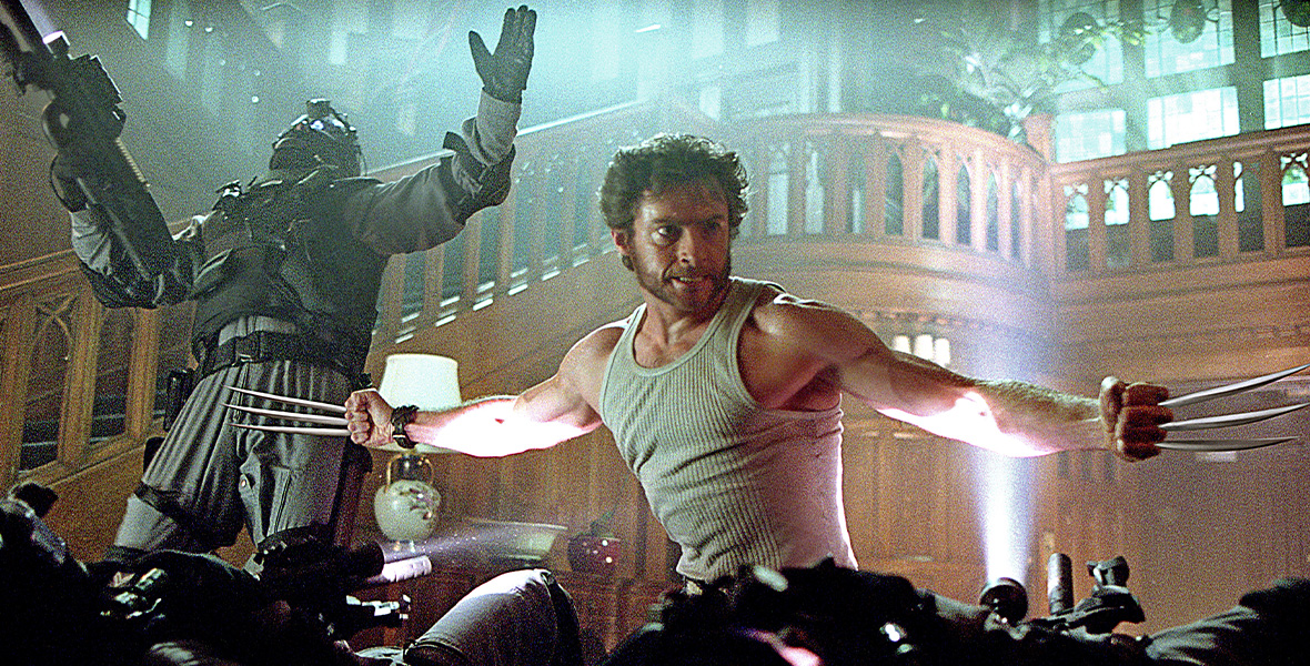In a scene from X2: X-Men United, actor Hugh Jackman portrays Wolverine and extends his arms outward. He wears a white ribbed tank top and has metal blades extending out of his knuckles. Behind him are a large wooden staircase and a masked fighter holding a large machine gun.