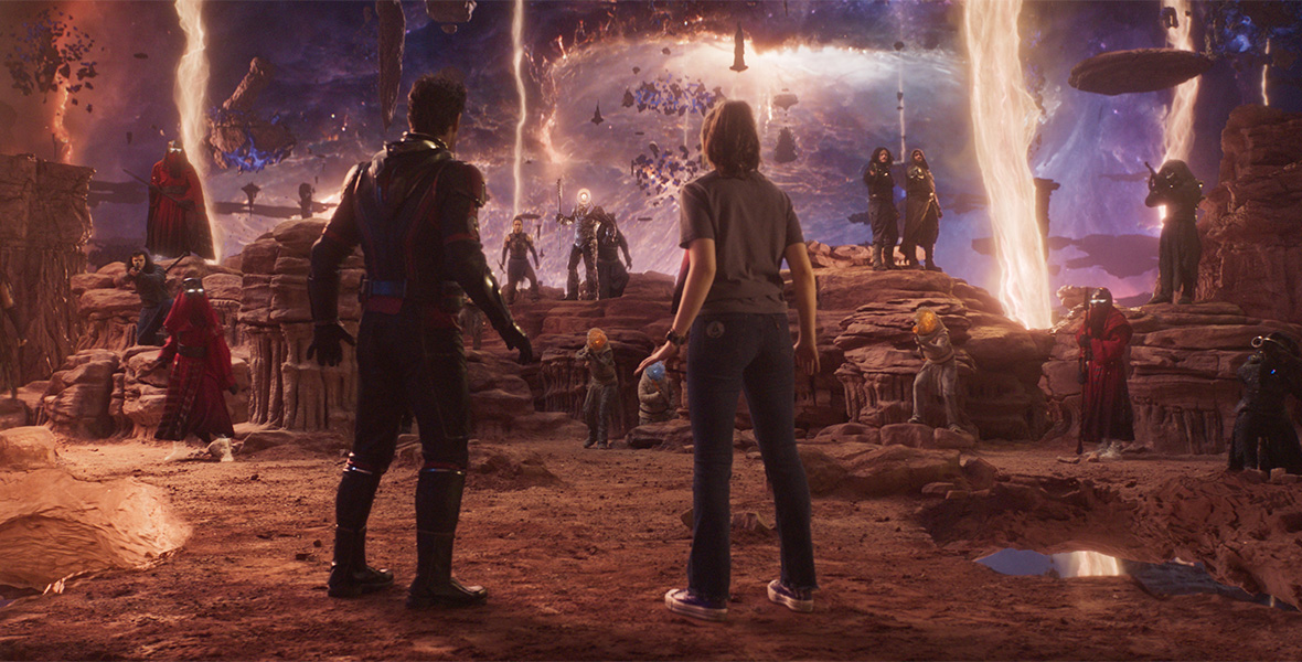 In a scene from Marvel Studios’ Ant-Man and the Wasp: Quantumania, actors Paul Rudd and Kathryn Lang look at a group of people aiming weapons at them on an alien planet resembling a desert landscape.