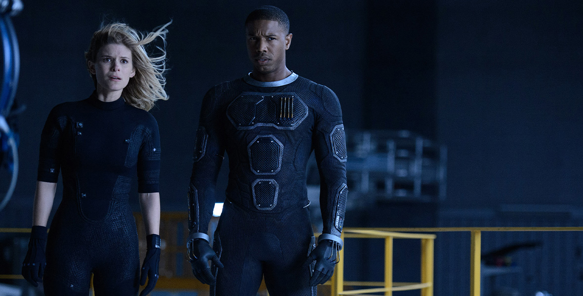 In a scene from Fantastic Four, actors Kate Mara as Sue Storm/Invisible Woman and Michael B. Jordan as Johnny Storm/Human Torch wear all-black ensembles and stand on a metal platform.