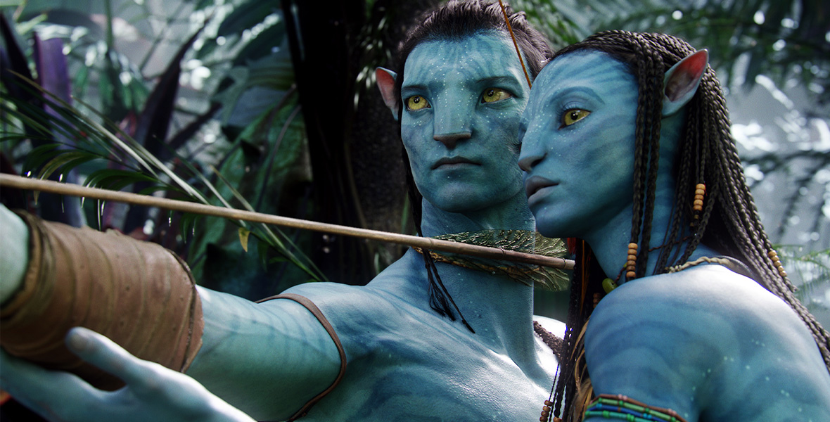 In a scene from 20th Century Studios’ Avatar, actor Zoe Saldaña portrays Neytiri, an alien being with blue CGI skin, golden yellow eyes, and long dark hair, and stands chest to chest with actor Sam Worthington as Jake Sully, in his alien form with blue CGI ski, golden yellow eyes, and dark hair. Worthington aims a large arrow. Saldana wears necklaces around her neck and left arms. Behind Saldaña and Worthington are neon strands cascading down and green foliage.