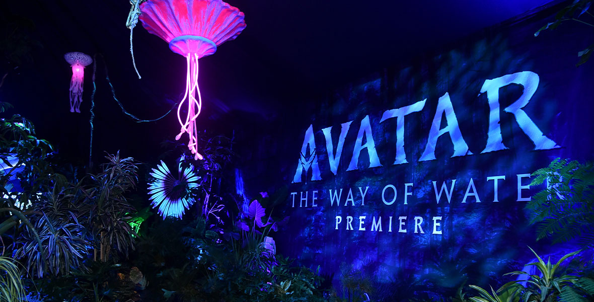 The entrance to the Avatar: The Way of Water premiere, which has been decorated to look like the rainforest of Pandora, with glowing flowers hanging from the ceiling. There is a wall on the right side with “Avatar: The Way of Water premiere” printed on it.