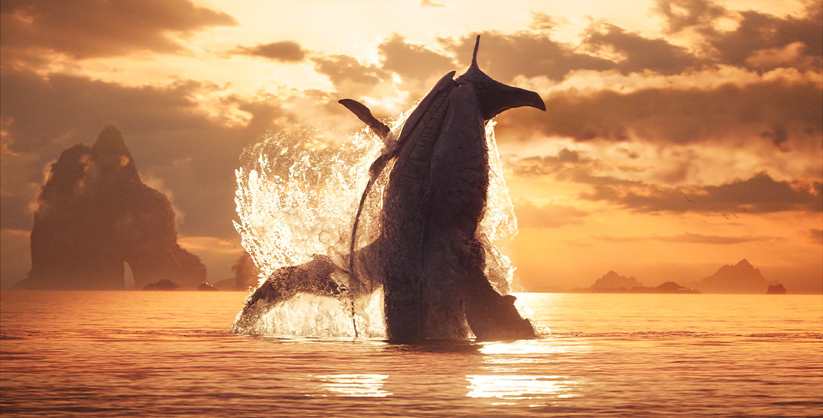 A whale-like creature called a Tulkun splashes above the water’s surface at sunset. Behind the Tulkun in the distance is a large rock formation.