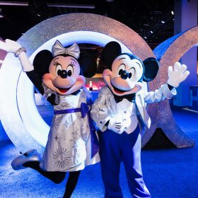 Minnie Mouse, on the left, and Mickey Mouse, on the right, strike a celebratory pose in their Disney100 platinum-colored outfits. They are standing in front of a giant walk-through rendition of the numeral 100, which served as the entryway to the Walt Disney Archives pavilion at the D23 Expo in September in Anaheim, California.