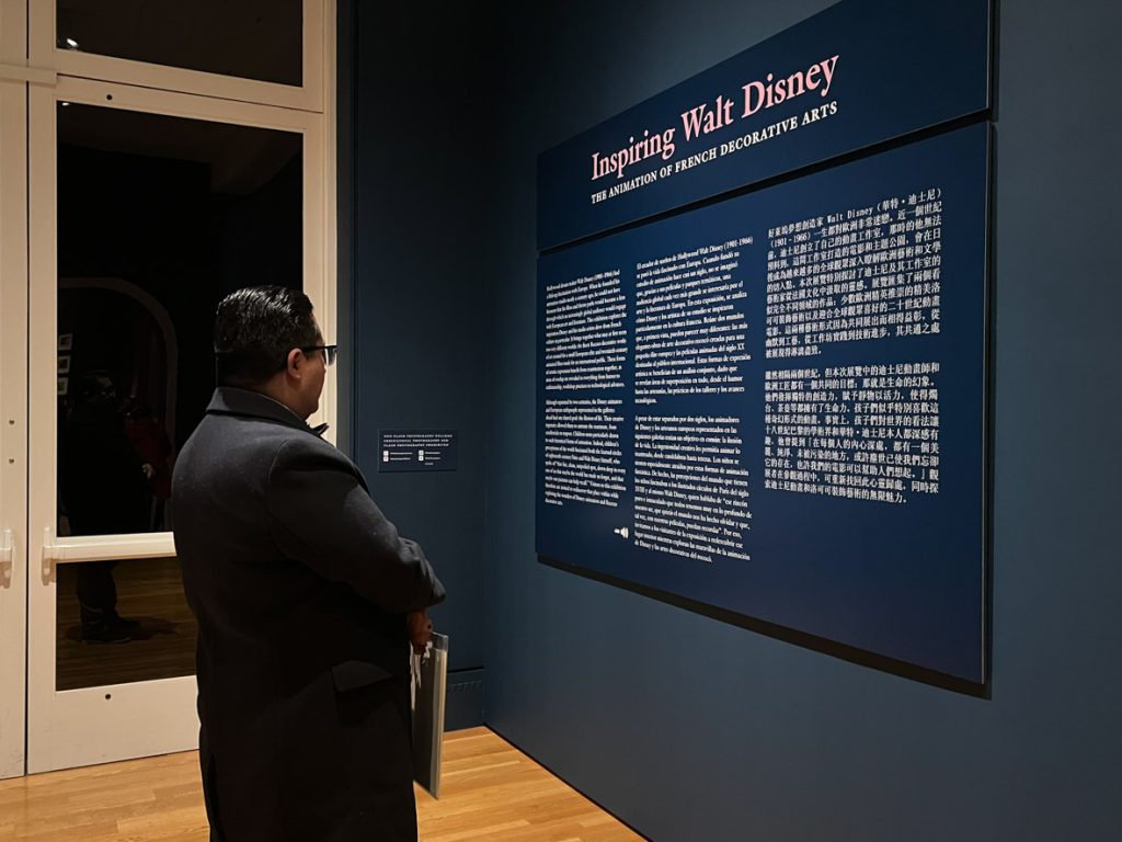 Guest reading the Inspiring Walt Disney placard. The guest is wearing a black coat.