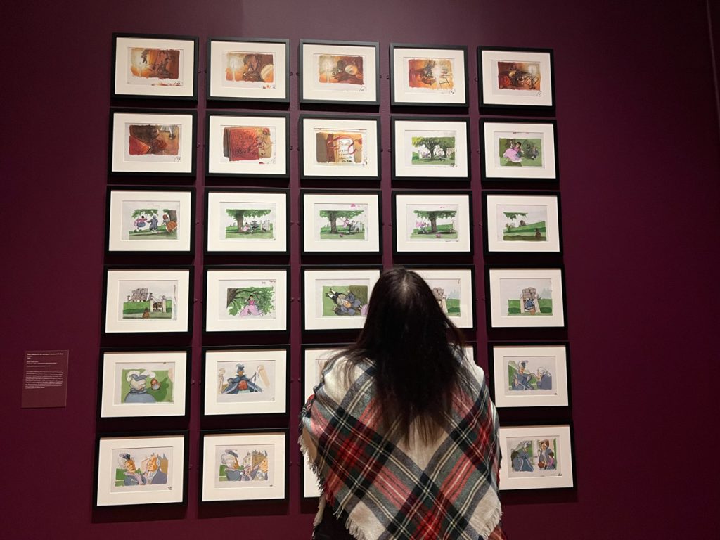 Guest looking at animation cell paintings. The guest is wearing a plaid wrap.