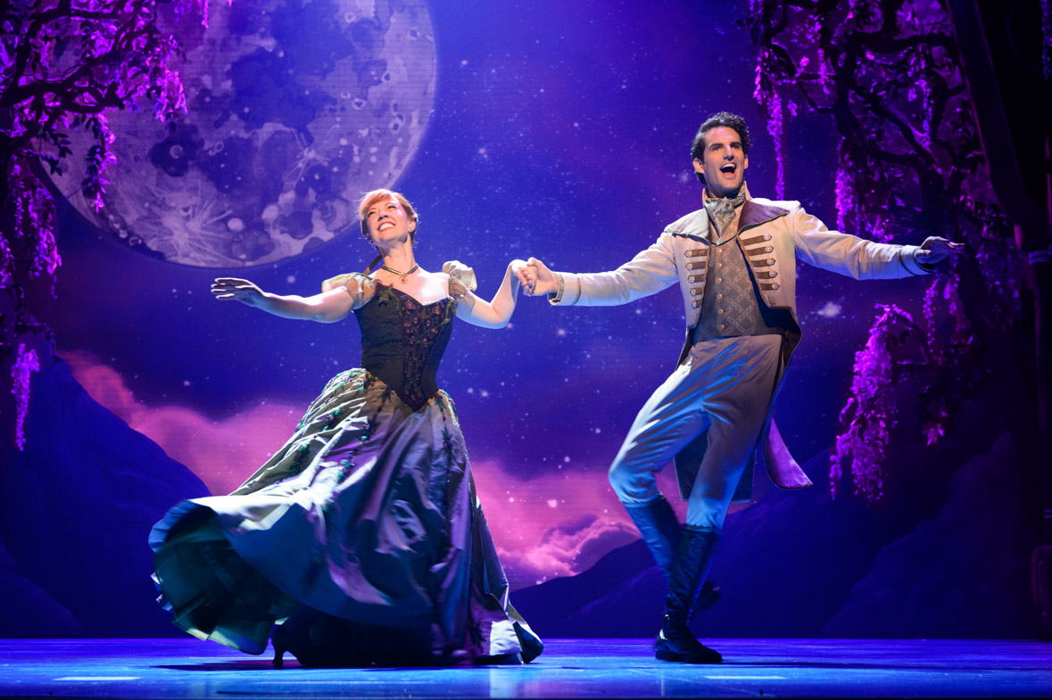 Patti Murin (Anna) and John Riddle (Hans) dance together against a purple night sky backdrop in Frozen.